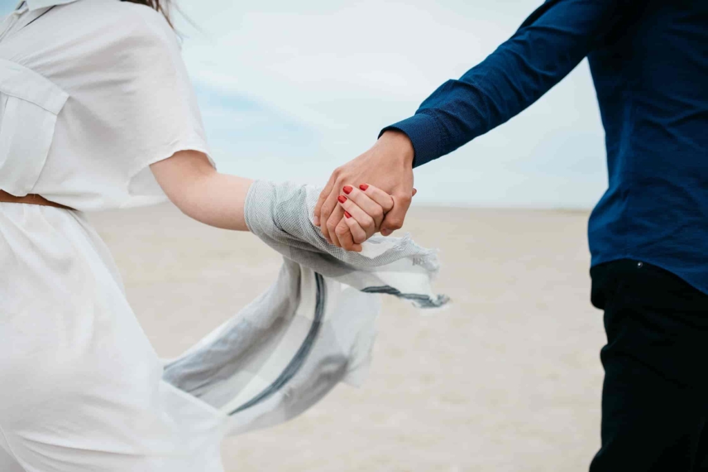 Two people holding hands at a beach.