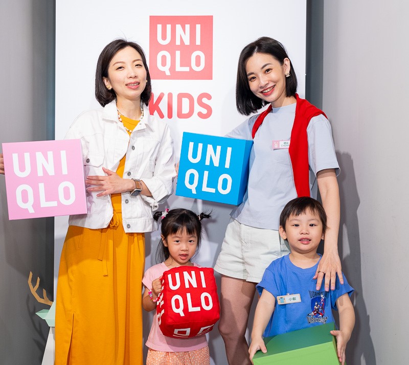 Two adults and two children holding UNIQLO signs, standing in front of a UNIQLO KIDS backdrop.