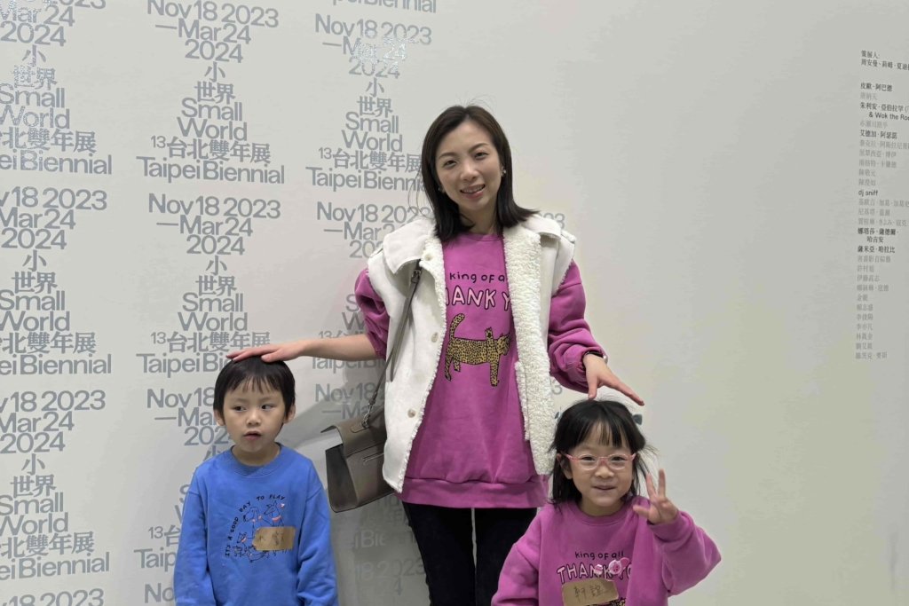 Three people wearing tops standing in front of a backdrop with texts.