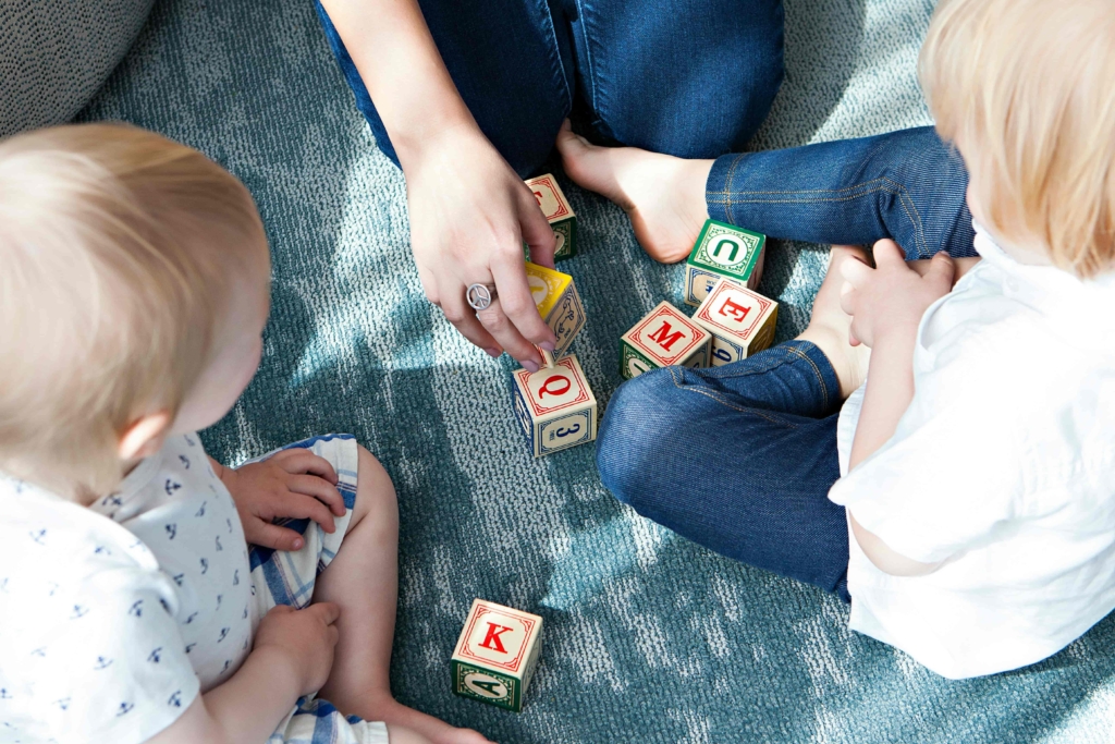 Two children and an adult playing with alphabet blocks on a carpet.